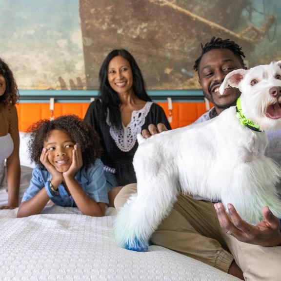 Family with dog on hotel bed at Hotel Indigo pet-friendly lodging in Orange Beach